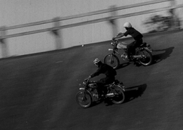 Dust and Metal. Black and White image of two people racing on motorcycles.